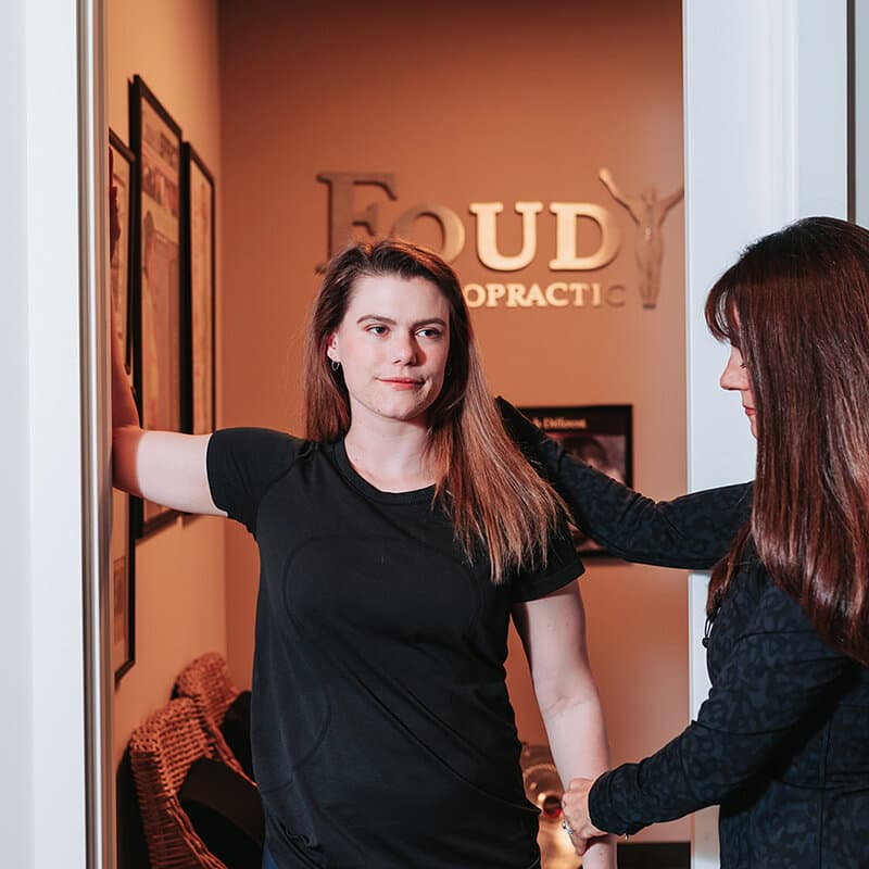 Team members at the Foudy Chiropractic logo wall in the office lobby